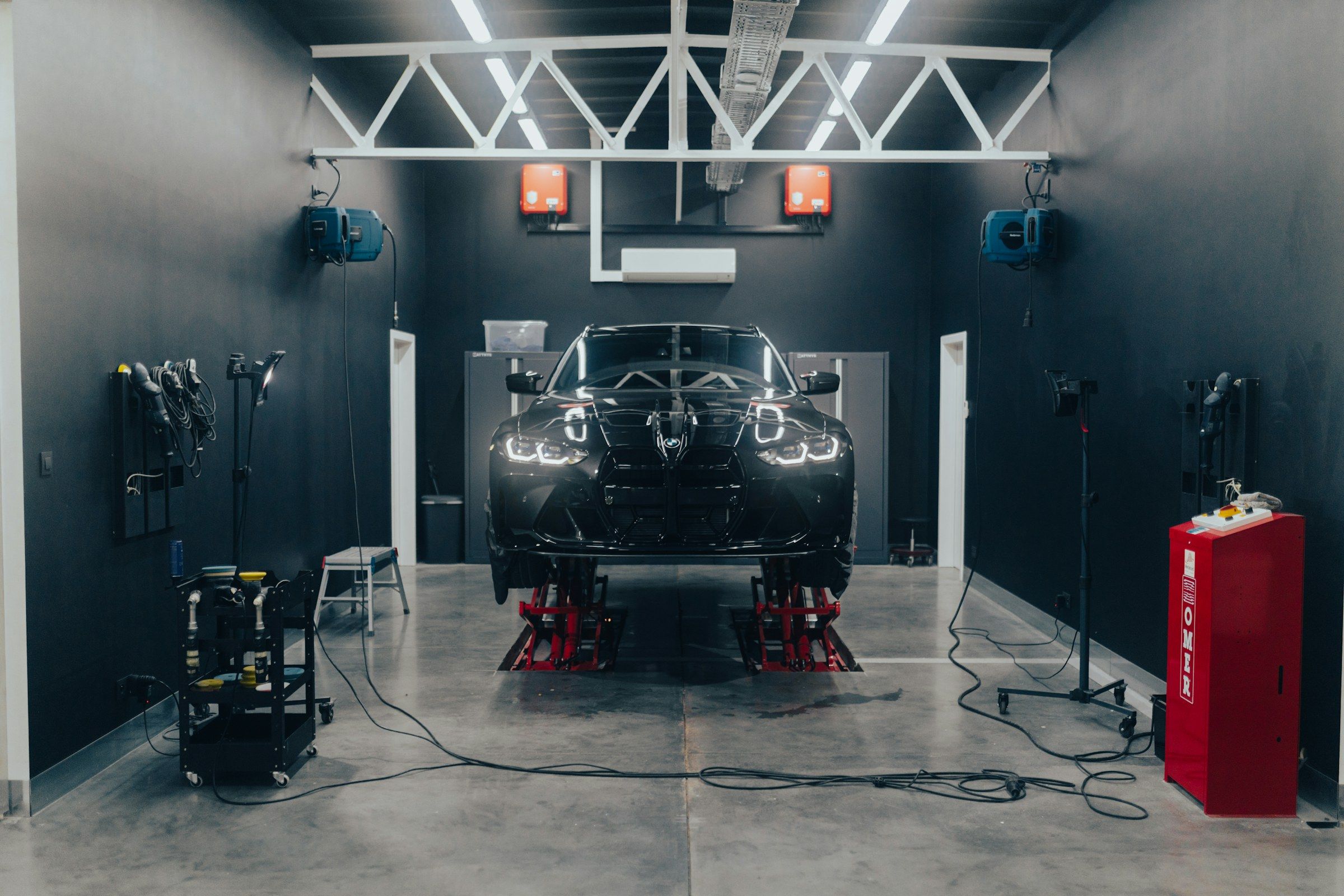 Car raised on a lift in a dark modern workshop with a red tool cabinet