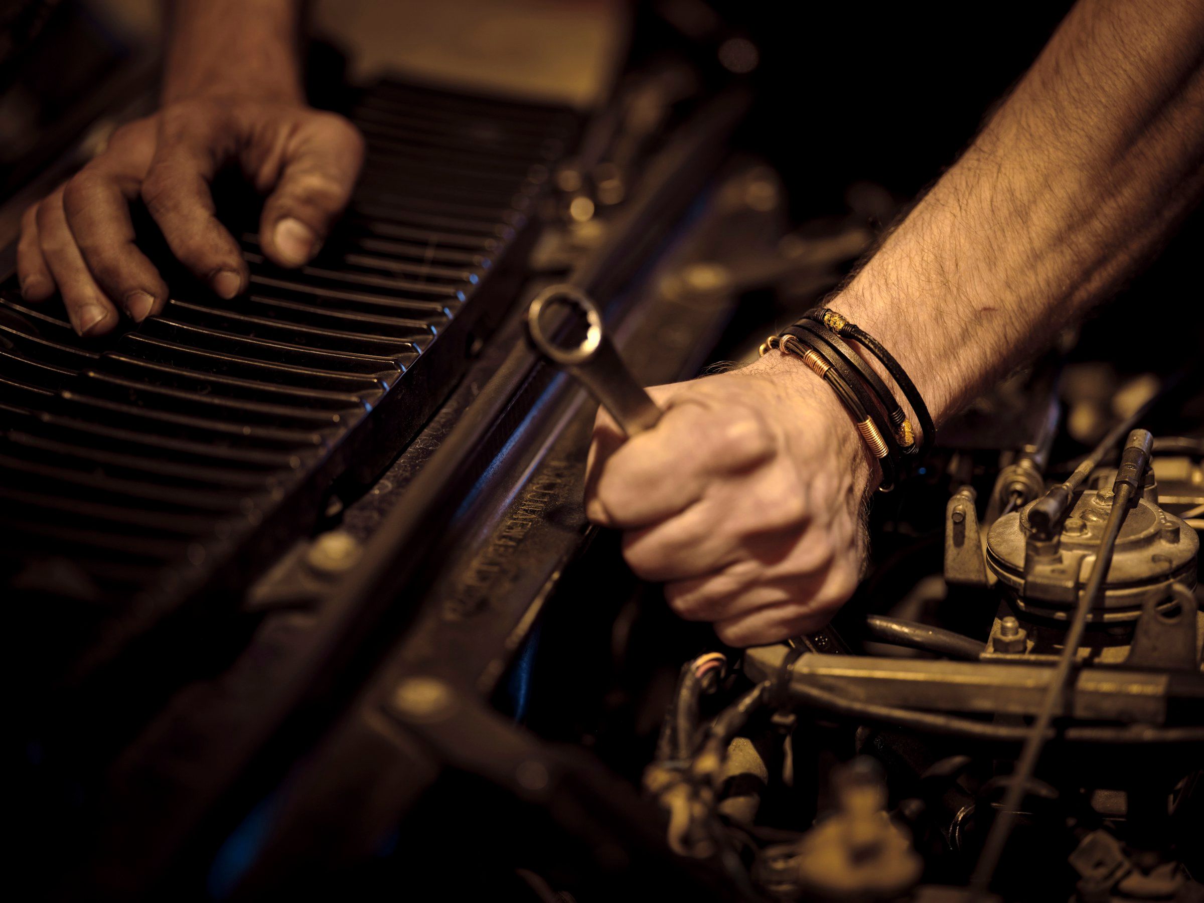 Grease-stained hands turning a wrench deep in an engine bay under warm light