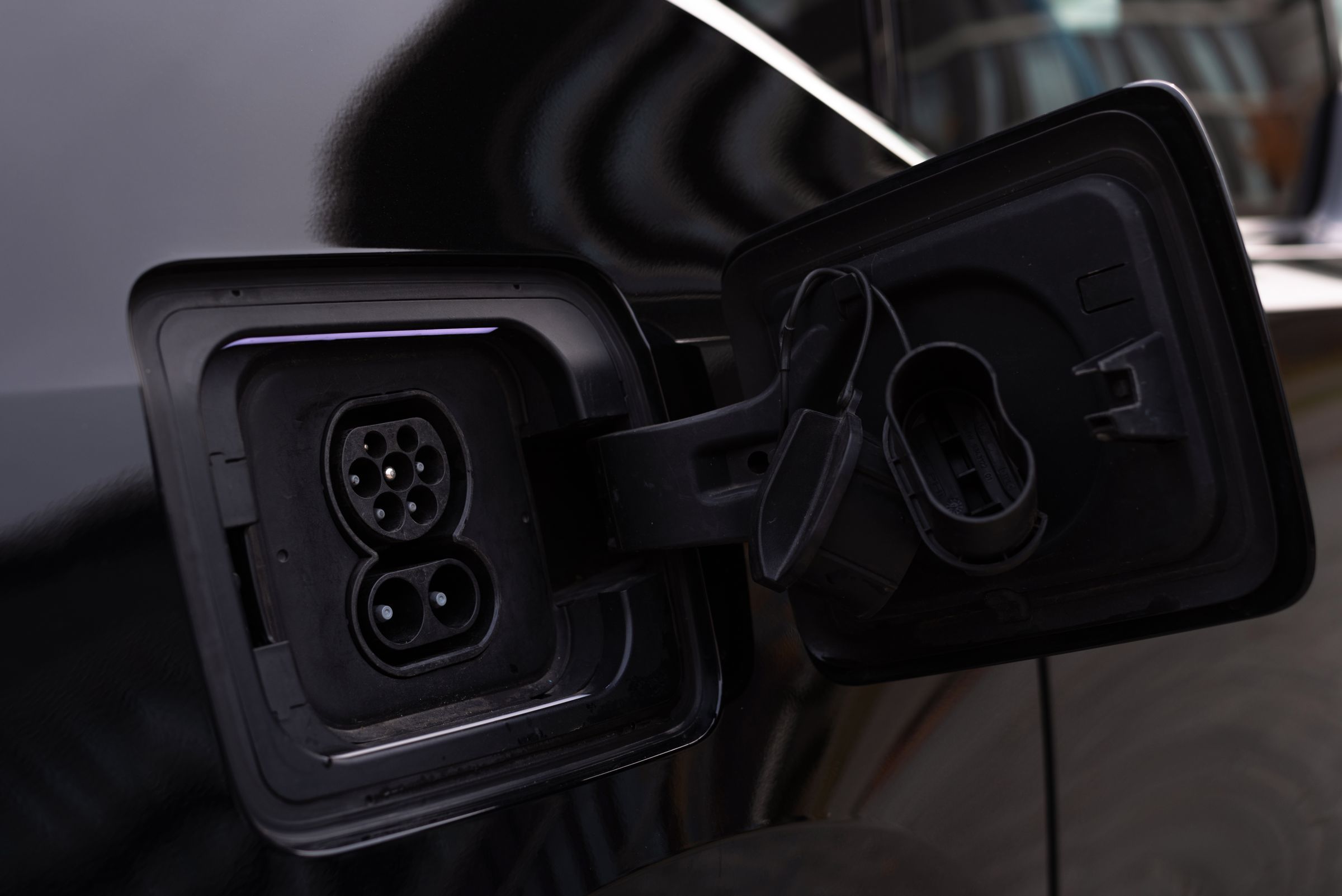 Open charging port flap on a dark plug-in car, showing the charging socket