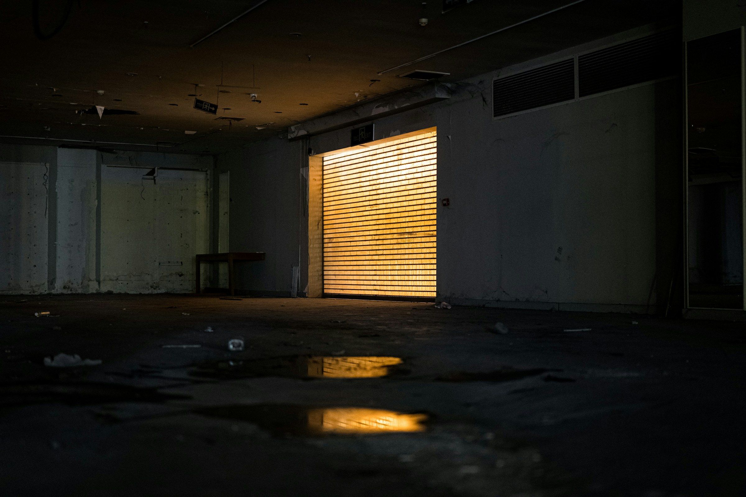 Empty garage bay at night, a roller door glowing amber at the far end and light reflecting in puddles on the floor