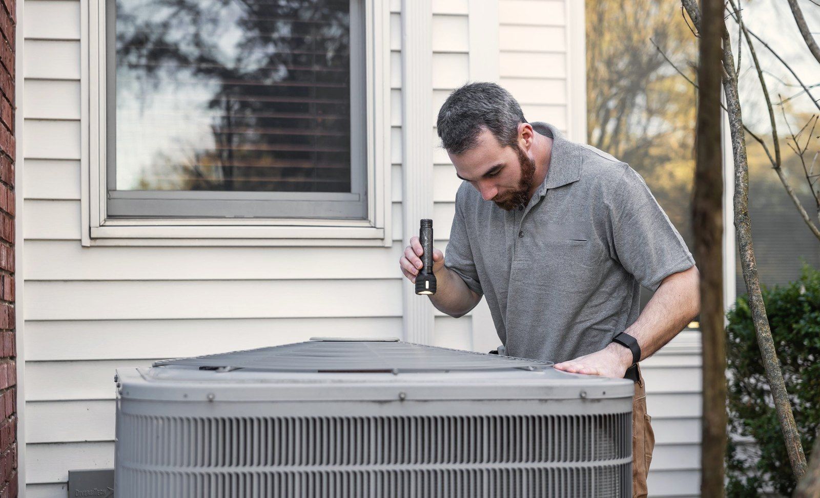 A technician inspecting an outdoor air conditioner beside a house
