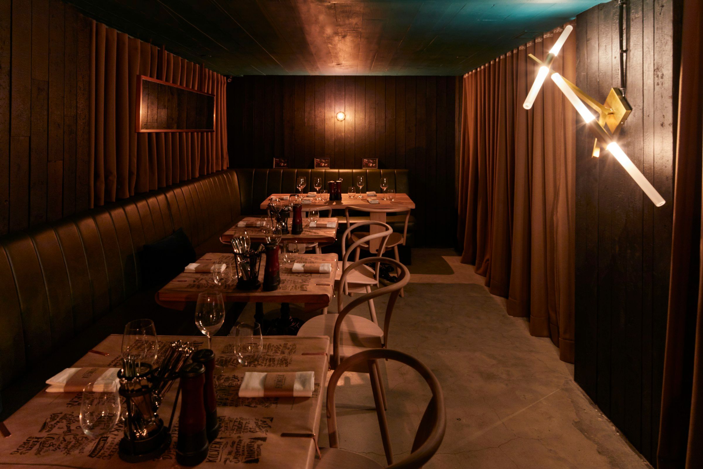 A dark wood-panelled dining room with set tables, a green banquette and velvet curtains in warm low light.