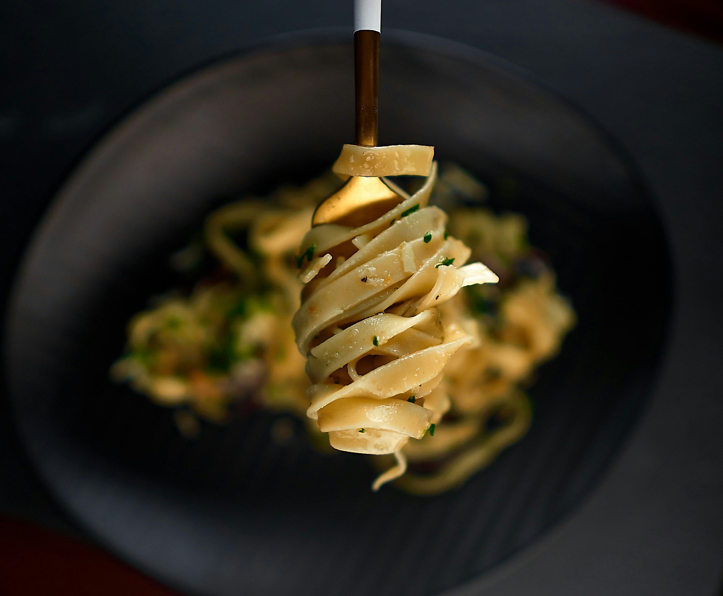 Ribbons of fettuccine twirled on a fork above a dark plate.