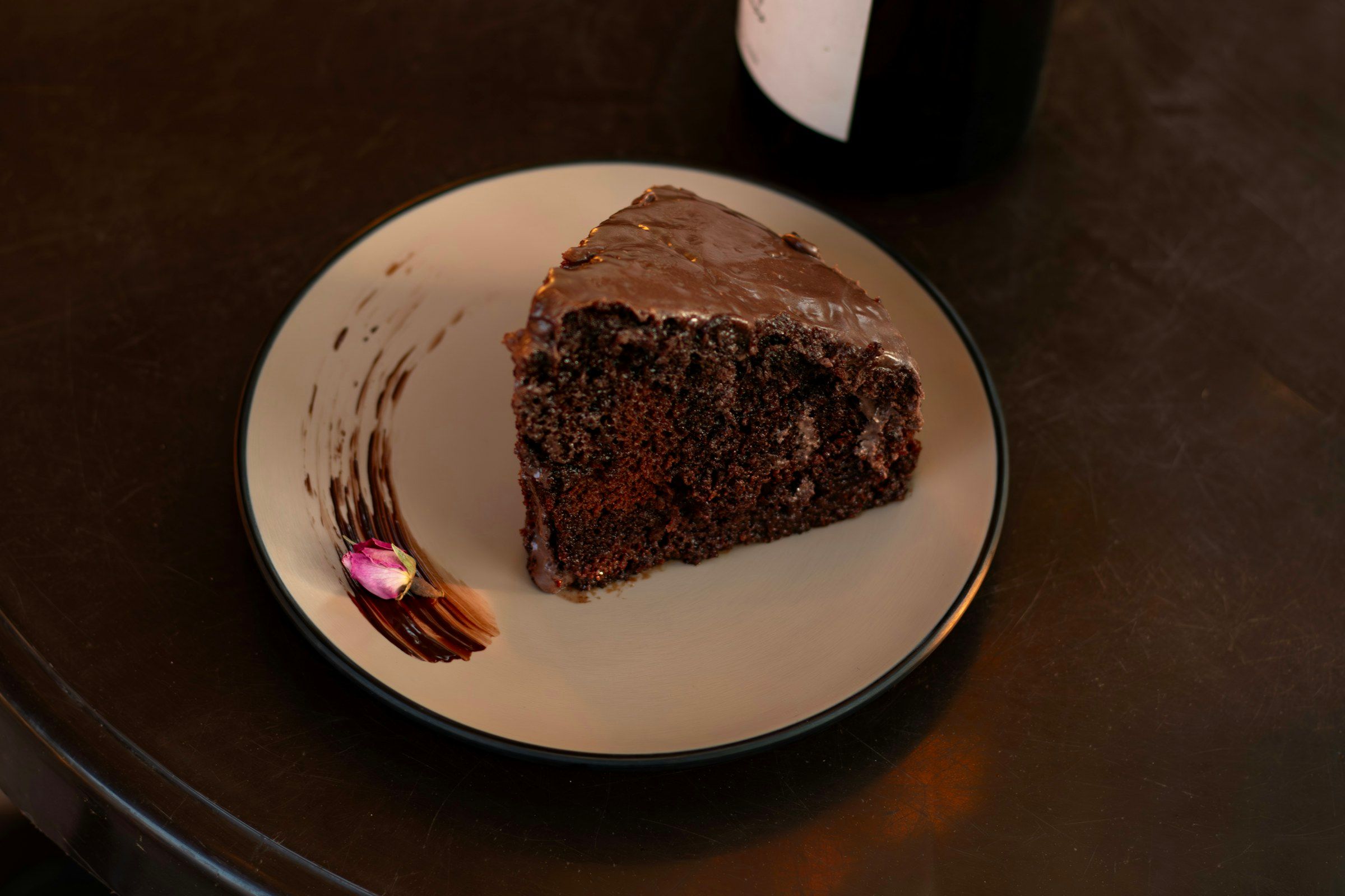 A slice of chocolate cake on a cream plate on a dark wooden table.