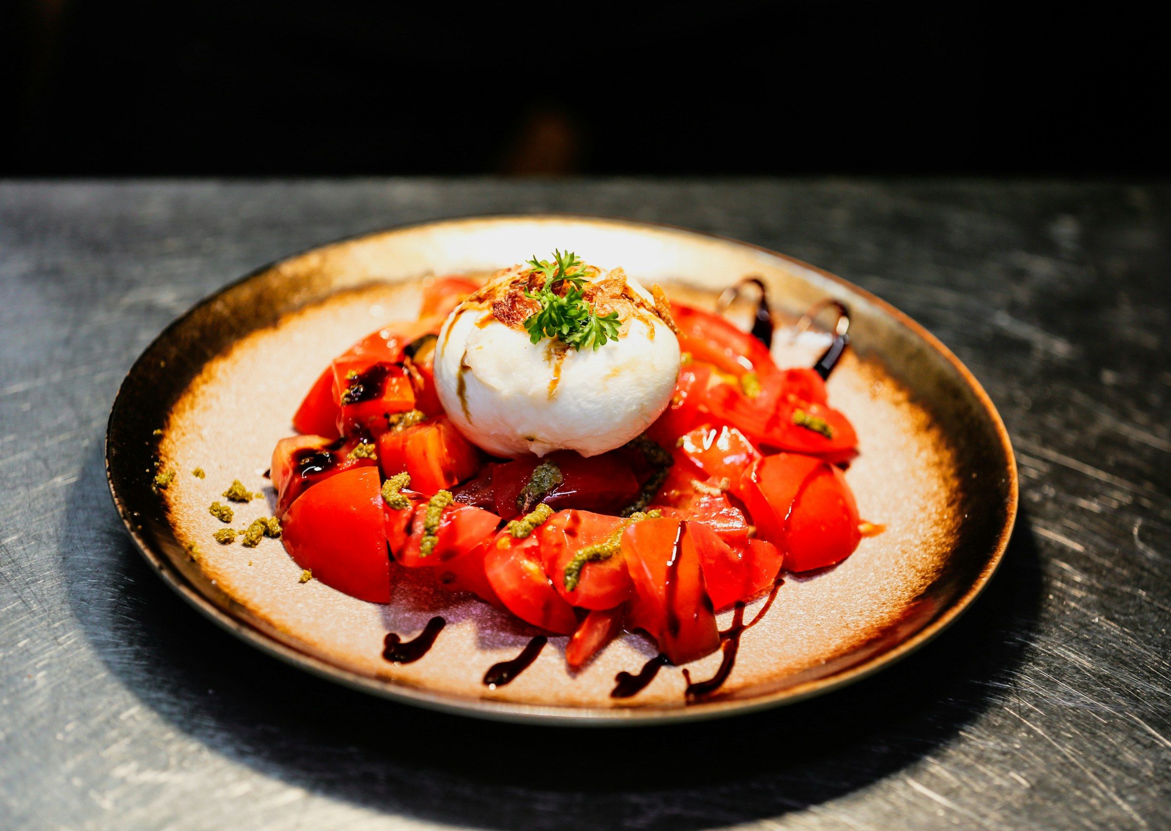 Burrata on sliced tomatoes with herbs and balsamic on a dark-rimmed plate.