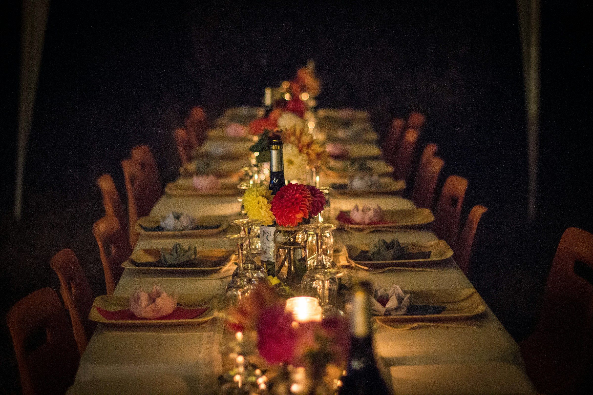 A long dinner table set for a party, with flowers, candles and wine glasses running its length in a dark room.